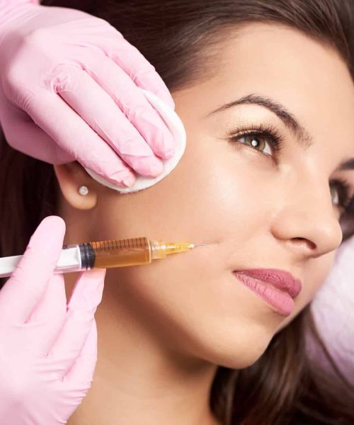 Close-up of beautiful woman getting injection in the cosmetology salon. Doctor in medical gloves with syringe injects cheeks drug.